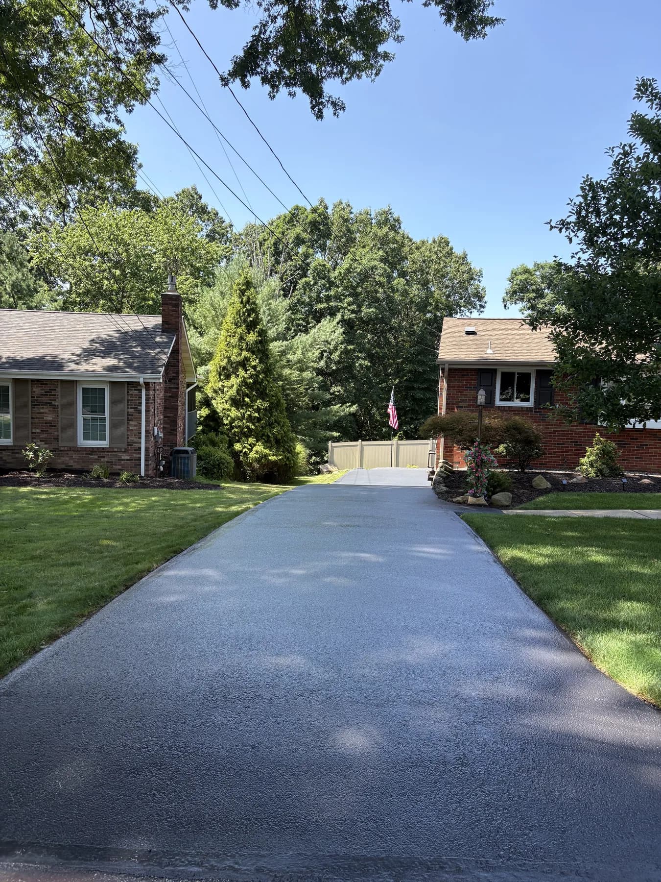 The same long driveway freshly hand-sealed with a glossy deep black finish
