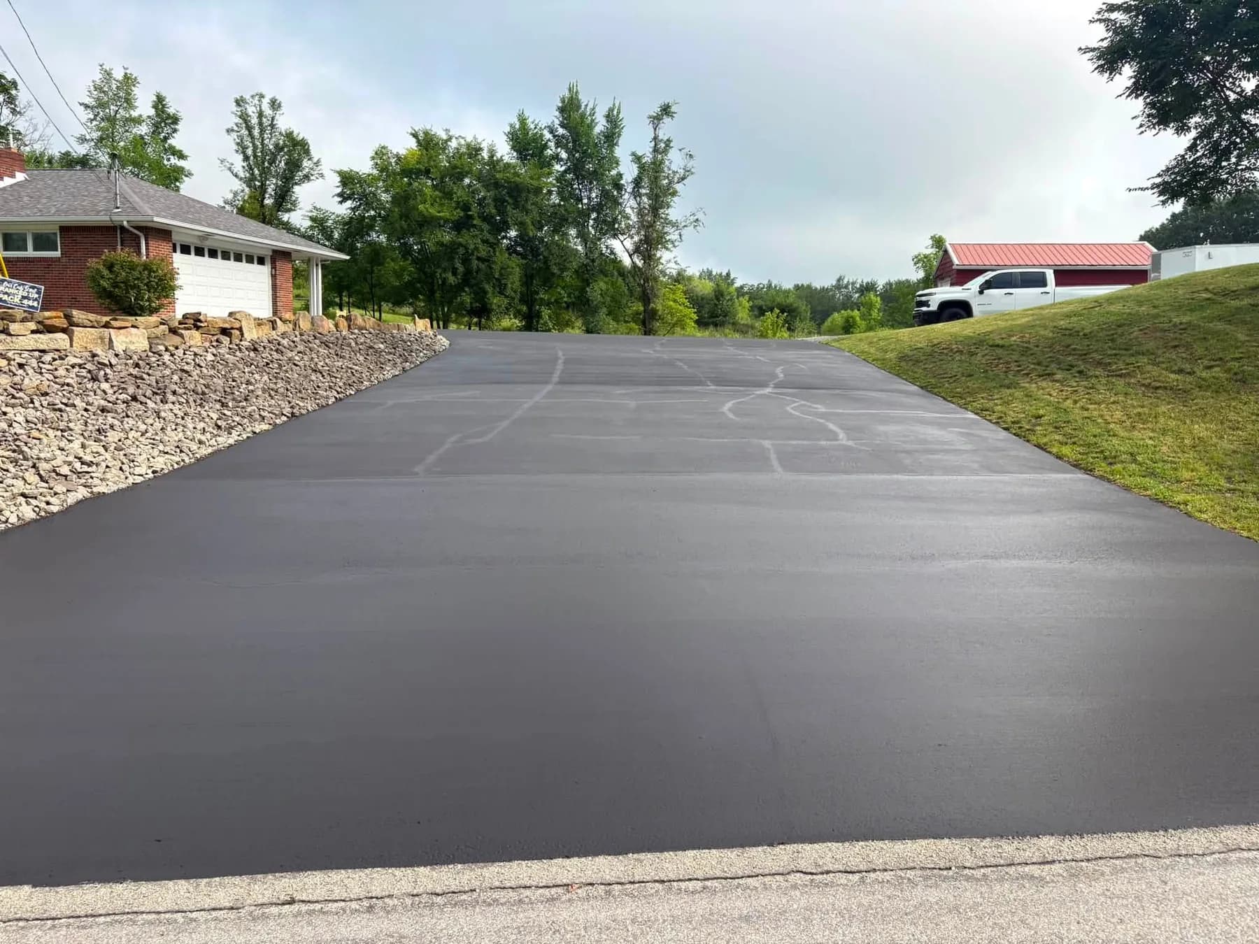 Freshly hand-sealed driveway edged by a stacked stone retaining wall